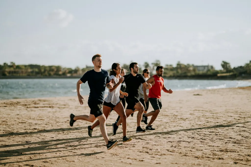Grupo de seis personas corriendo juntas por la arena, junto a la orilla