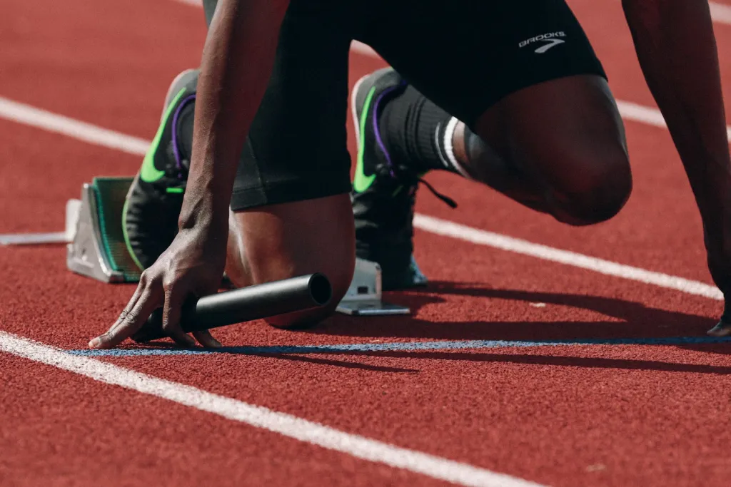 Atleta en los tacos de salida de una pista, con el testigo de relevos en la mano