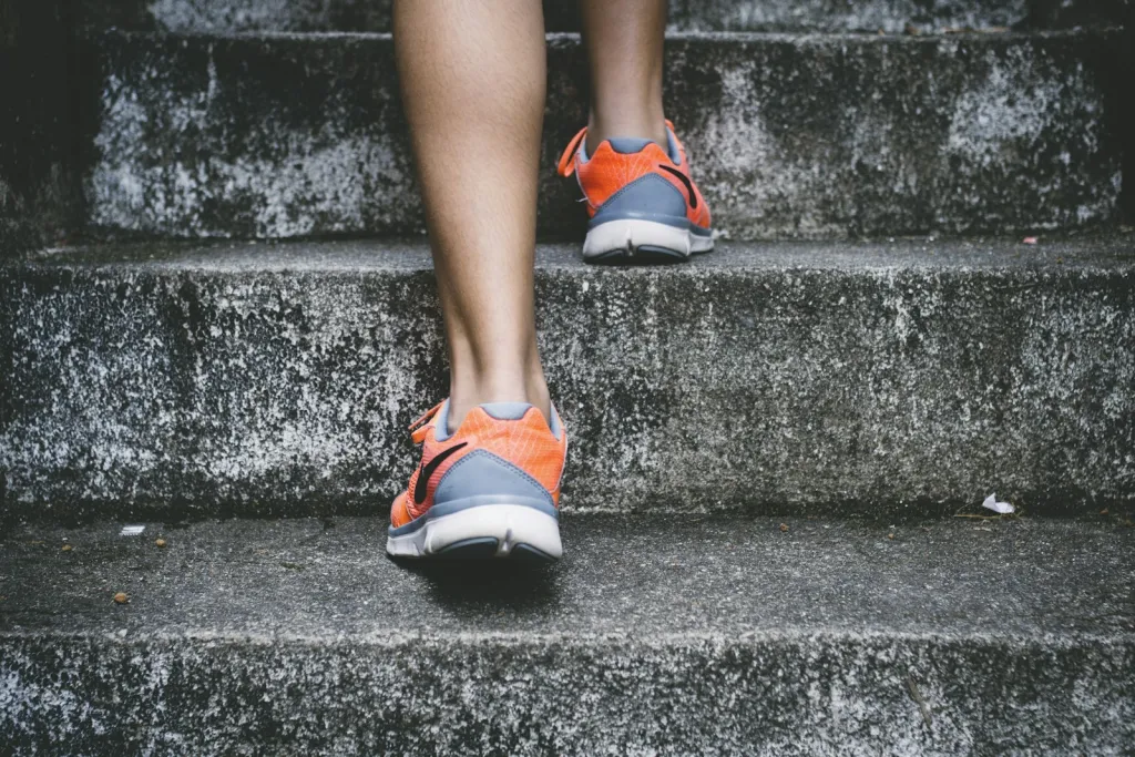 Piernas de una persona subiendo unas escaleras de hormigón con zapatillas de correr